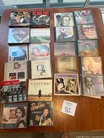 Top-down photo showing approximately 30 CDs arranged tightly on a wooden table. Various cover arts visible including Big Band Fever, Julie London, Ethel Merman, Glen Miller, and more.