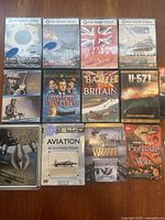 Photo showing all 12 DVDs arranged on a wooden surface, visible titles and covers include PBS Home Video war documentaries, Fox War Classics, and aviation collections.
