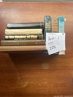 Top view of 7 vintage hardcover books, spines showing titles and authors, arranged horizontally on wooden surface.