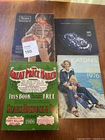 Four catalogues laid out on a wooden surface including Eatons and Sears catalogues plus 1906 replica book