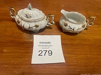 Photo showing the two-piece hand painted cream and sugar set with gold accents on wooden table.