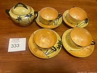 Photo showing four tea cups with matching saucers and one sugar bowl grouped on a wooden surface, all with palm tree and camel silhouette design.