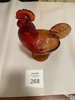 Side and front view of vintage red-orange glass candy dish shaped like a rooster with textured feathers and comb. Pedestal base visible.