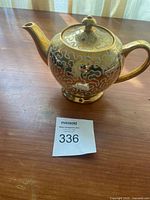 Photo showing vintage Sadler gold teapot from the front with handle and spout visible on wooden table