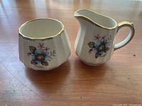 Photo showing vintage Sadler sugar bowl and creamer with floral patterns and gold trim on a wooden surface.