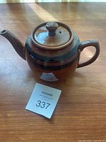Side view of vintage Sadler teapot showing spout, handle, lid with knob, and brown stripe on ceramic body on wooden surface.