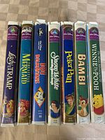 Eight Disney VHS tapes in original cases arranged side by side, titles visible on spines and front covers: Lady and the Tramp, The Little Mermaid, 101 Dalmatians, Snow White and the Seven Dwarfs, Peter Pan, Bambi, Winnie the Pooh.