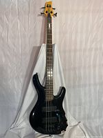 Full front view of a black Ibanez electric bass guitar with four strings and visible damage on body edges.