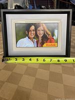 Front view of Kodak P720 digital photo frame displaying an image of two people, with measurement tape showing around 8.5 inches width.