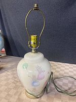Full view of lamp showing ceramic body with bunny illustrations and metal base, electrical cord visible.