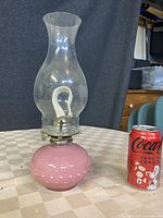 Full view of pink glass oil lamp next to a Coca-Cola can for size reference, showing rounded hobnail textured base and clear glass chimney.