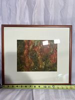 Framed watercolor painting with a measuring tape showing the artwork size at about 12 inches wide. Wood frame and matte border are visible. The painting has earthy colors and an abstract forest theme.