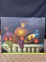 Full front view of signed still life oil painting with table, fruits, jug and jar, measuring approximately 20 inches wide.