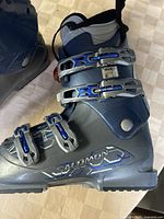 Photo showing left side of a Salomon ski boot in blue and gray with three silver and blue buckles and branding on the side.