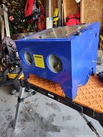 Front and side view of blue cabinet sitting on work surface showing glove ports and warning label