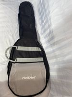 Front view of soft side guitar case laid flat on a white surface showing main compartment and front pocket with First Act logo.