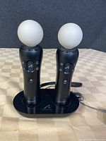 Two Sony PlayStation Move motion controller wands on a charging dock with spherical white tips visible and buttons on handles.
