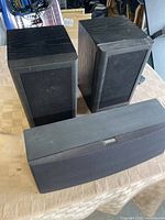 Two black Mission bookshelf speakers and one Yamaha center channel speaker on a table.