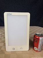 Clear front view of the Verilux light therapy lamp next to a soda can for size reference, shows white rectangular frame and unlit panel.