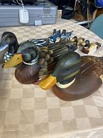 Seven wooden duck figurines arranged on a beige patterned surface, three large and four small with diverse paint details.