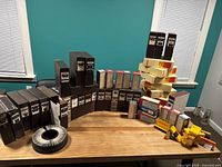 Wide shot showing multiple Kodak brown slide boxes, beige Kodak Carousel 140 slide tray boxes, and several smaller slide changer boxes arranged in a curve on a wooden table under a teal wall background.