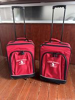 Front view of two red Walt Disney World rolling suitcases with telescoping handles extended and external pockets with Disney logo on front.