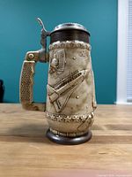 Side view of beige ceramic beer stein with embossed space shuttle and stars, showing metal hinged lid and textured handle.