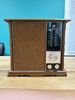Front view of vintage RCA radio, showing maple wood finish and brown fabric speaker area with tuning and volume control knobs.