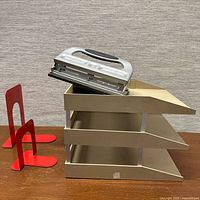 Overall view: two red bookends, beige three-tier filing tray, silver three-hole punch stacked on trays