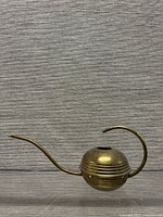 Side view showing full profile of brass watering can with curved spout and handle