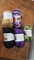 Photo showing five skeins of acrylic metallic ruffle yarn in assorted colors on a wooden surface.