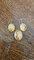 Photo showing pair of oval glass earrings and matching pendant with floral design on wood grain surface.