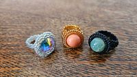 Front view of three large beaded rings featuring Swarovski crystals and natural stones on a wooden surface.