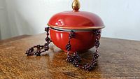 Garnet beaded necklace partially draped over a reddish-orange ceramic pot with lid, showing cluster bead detail.