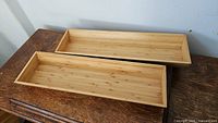 Top view of two rectangular bamboo trays placed on a wooden surface, showing the natural bamboo finish and slightly raised edges.