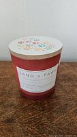 Front view of pink Sand + Paws scented candle with Coconut & Palm label and wooden lid with colorful paw prints.
