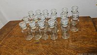 Full view of all 17 clear glass bottles with stoppers arranged in rows on a wooden surface.