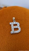 Front view of sterling silver letter B pendant with cubic zirconia stones set closely on surface.