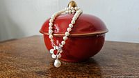 Sterling silver pearl necklace draped over a red round trinket box, showing the pearl strand and clasp detail.