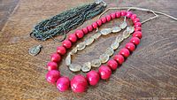Full set of four jewelry pieces laid out on wooden surface: multi-strand glass beads, citrine beads, large pink wooden beads, medallion pendant.