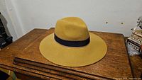 Beige wide brim fedora hat by Zara on wooden table, showing full shape and black band detail.