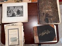 Top view showing several large prints and bound volumes on a wooden table. British Gallery Engravings volume cover is heavily worn. Large loose prints with classical engraved scenes are visible.