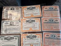 Photo showing seven antique railroad bond and stock certificates with ornate borders and varying colors (orange, beige). Included are certificates from The Pennsylvania Railroad Company, The Reading Railroad Company, and others.