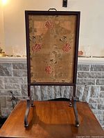 Full view of antique firescreen showing rectangular floral fabric panel and wooden frame with curved legs.