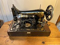 Side view of the Singer sewing machine showing the black body with gold decals, handwheel, and attached electric cord and bulb.