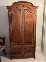 Full front view of tall antique wooden wardrobe with solid wood paneled doors and carved molding crown.