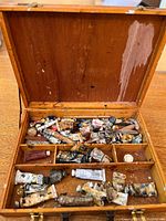 Wooden box with multiple compartments, containing many oil paint tubes in worn and used condition with some paint stains on box interior.
