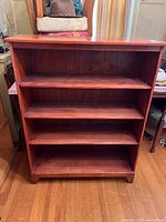 Front view of a cherry-colored solid wood bookshelf with four shelves.