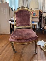 Front view of antique chair showing pink velvet seat and back, gold carving on frame