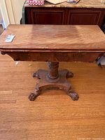 Full top and side view of a clawfoot antique wooden games table showing the rectangular top, pedestal, and part of the clawfoot base.